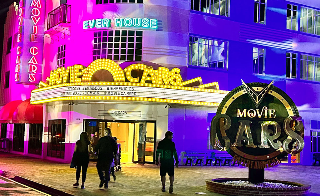 Entrada iluminada do Movie Cars no Wonder Park Foz, com fachada em neon brilhante e visitantes se aproximando da entrada, destacando a atmosfera vibrante e temática do parque.
