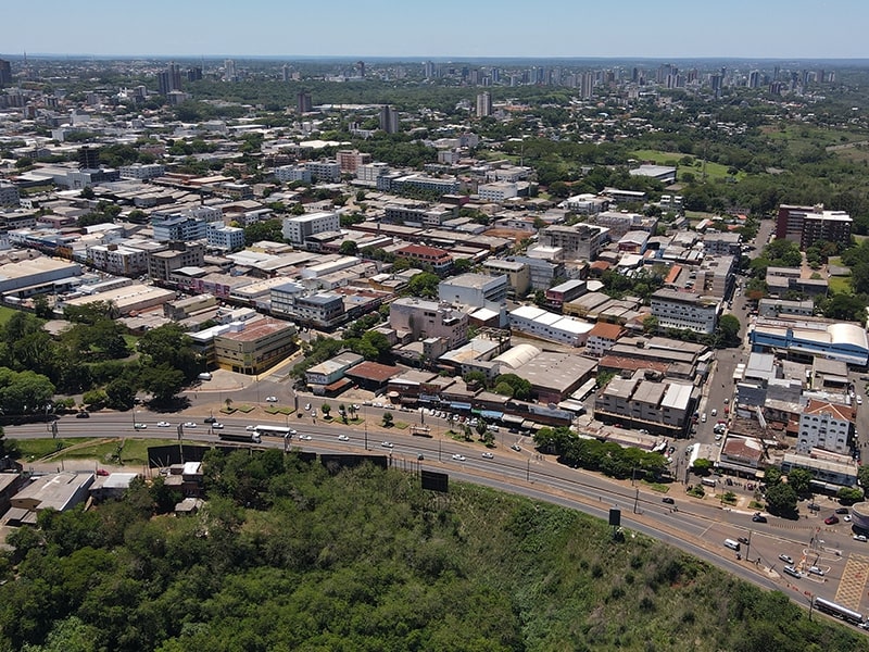 Vista aérea de uma área central de Foz do Iguaçu, destacando uma área urbana com várias construções e vias principais. A paisagem verde ao redor contrasta com o centro movimentado, sugerindo proximidade de um hotel em Foz do Iguaçu no centro da cidade.